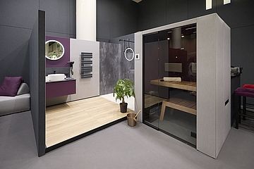 in modernes Badezimmer-Set mit minimalistischer Ausstattung. Zu sehen sind eine Dusche, ein Waschtisch mit rundem Spiegel, ein kleiner Pflanzenkübel und eine integrierte Sauna mit gläserner Front.